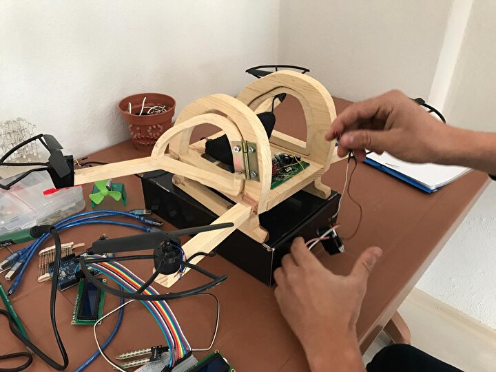 Ahşap bir drone gövdesinin masada elektronik bileşenler ve kablolarla birleştirildiği yakın çekim belgesel fotoğraf, sıcak tonlarda ahşap ve metal dokusu.